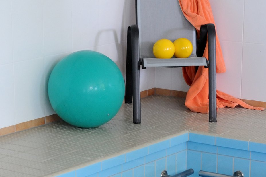 Ein großer Gymnastikball und zwei kleine Bälle auf einem Stuhl am Schwimmbeckenrand
