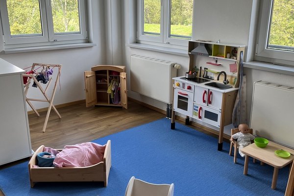 Man sieht eine Puppenspielecke mit Kinderwagen, Einkaufsladen und anderen Gegenständen