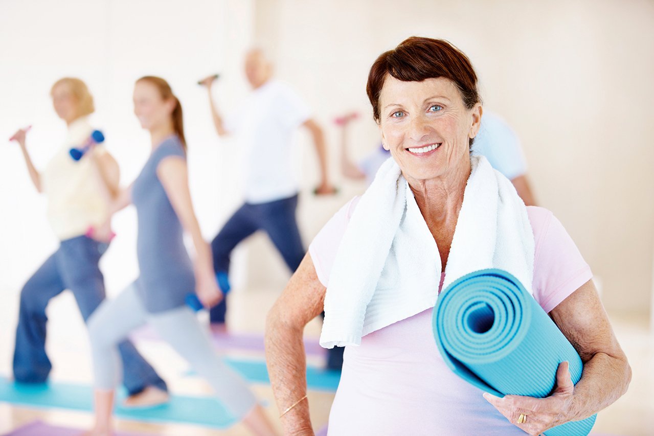Eine lächelnde Seniorin mit einer Yogamatte in der Hand 