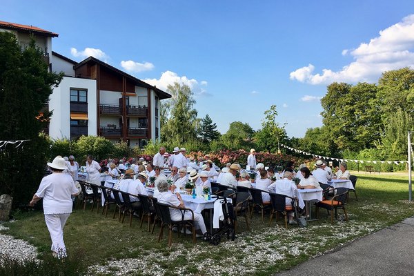 Senior*innen in weißen Klamotten sitzen an großen Tischen 