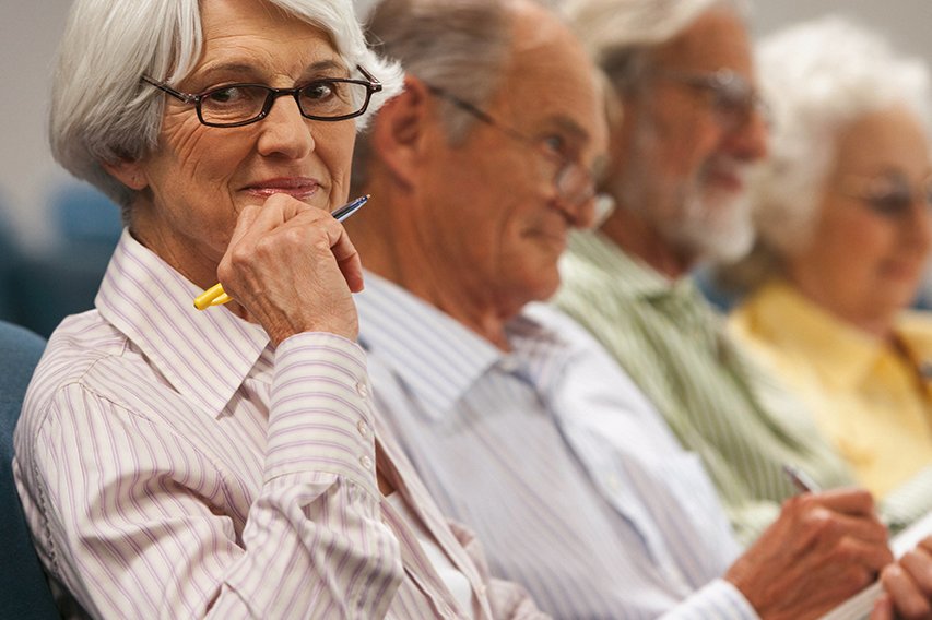 Vier Senior*innen sitzen mit Stift und Papier in einem Saal