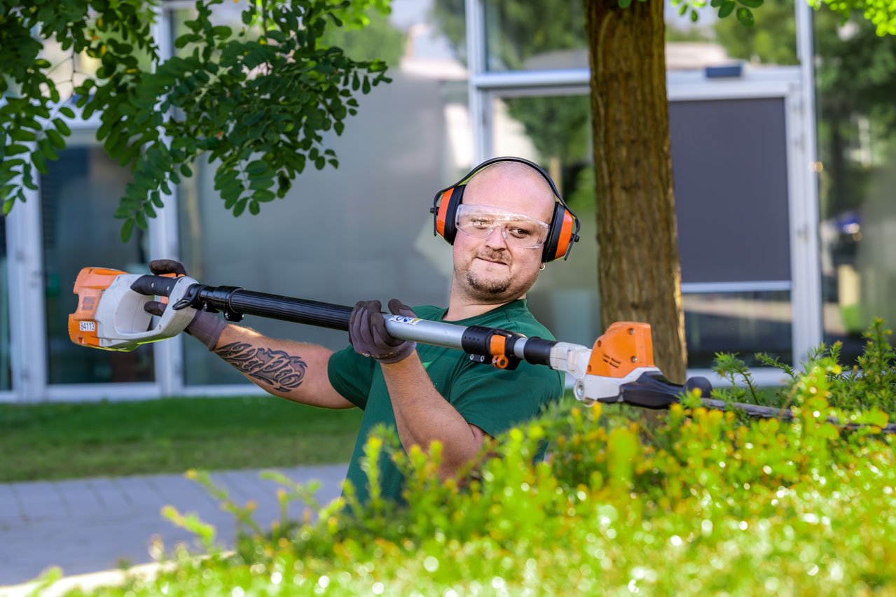 Ein Klient der Augustinum Gärtnerei Hollern schneidet mit einer akkubetriebenen Teleskopheckenschere die Hecke