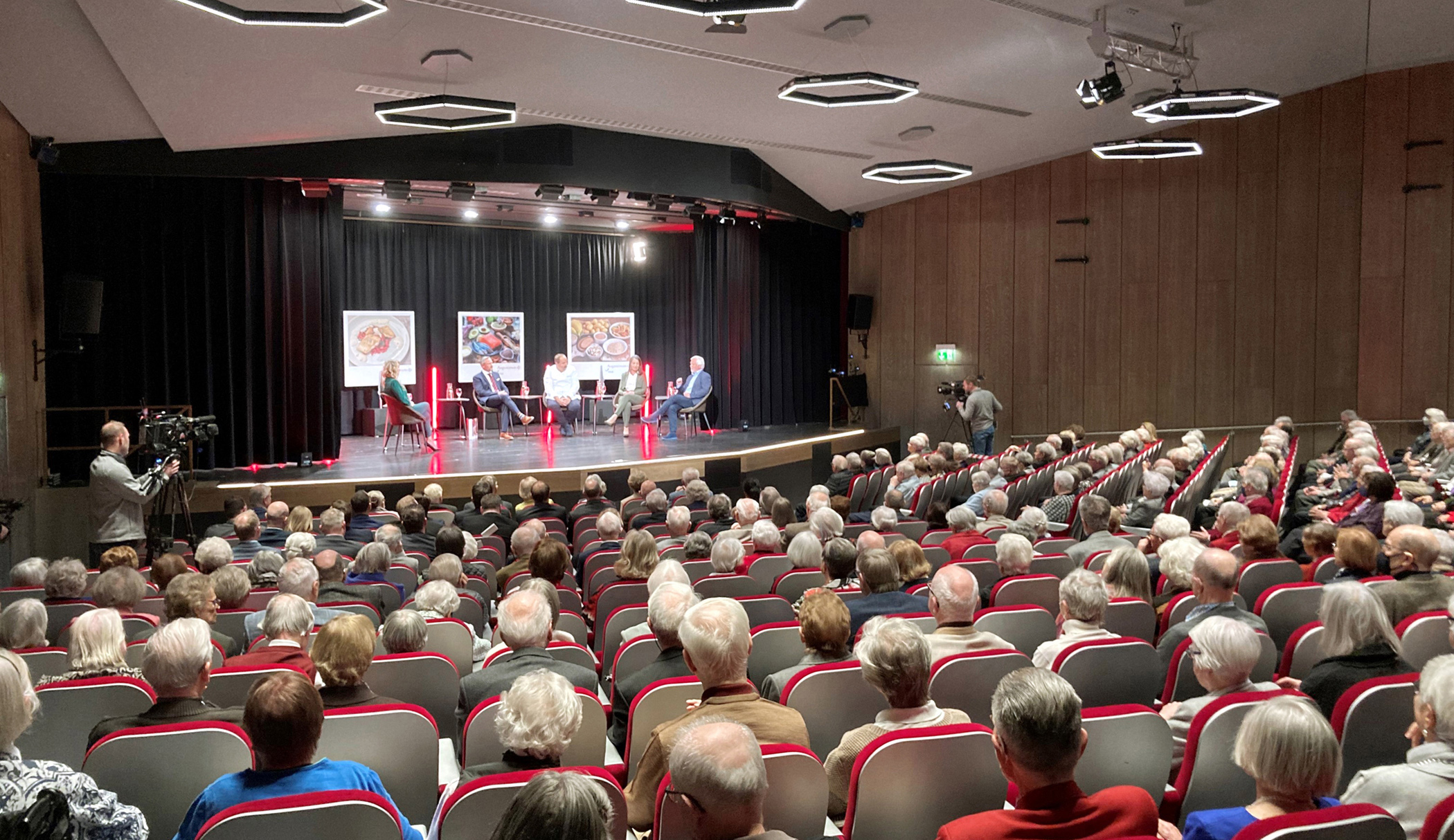 Senior*innen sitzen im Theatersaal während sich fünf Leute auf der Bühne unterhalten