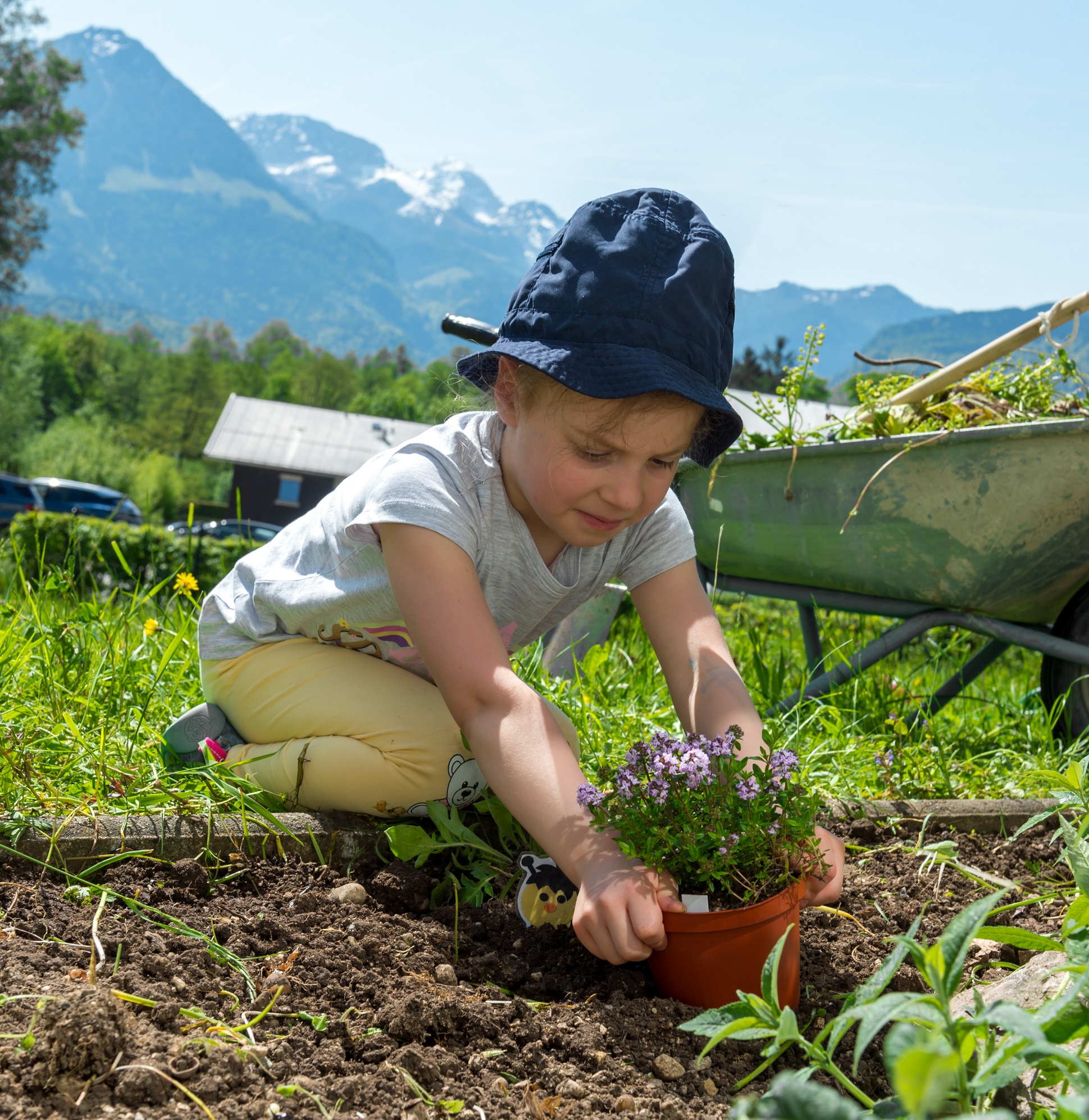 Ein Kind sitzt in einem Garten und pflanzt eine Pflanze ein 