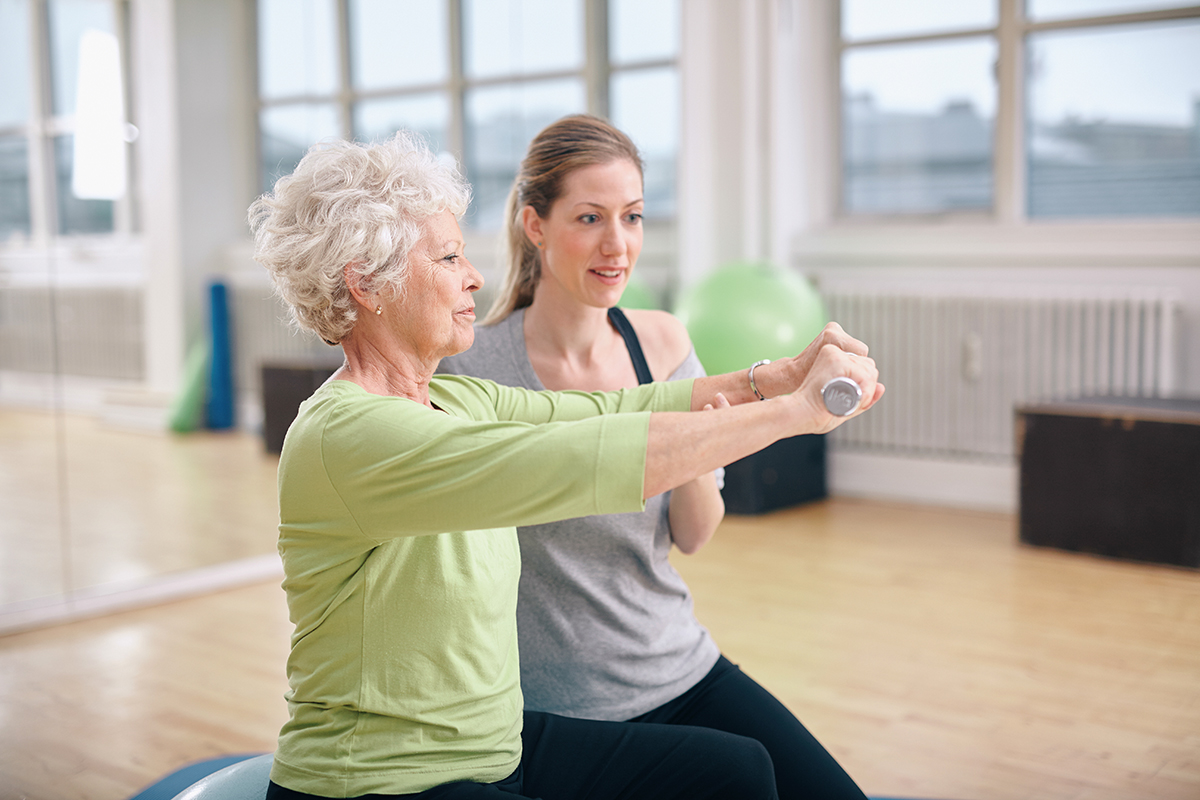 Eine Trainerin hilft einer Seniorin bei einer Gymnastik-Übung