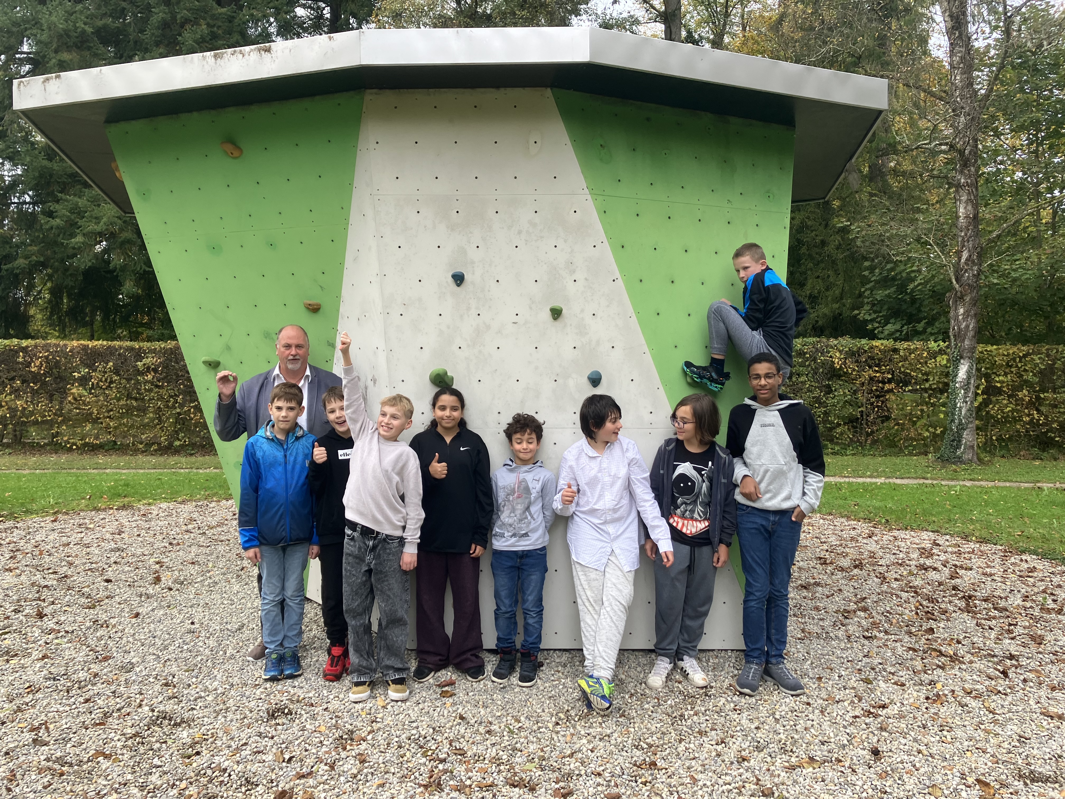 Ein Erwachsener und Schüler*innen stehen vor einer Boulderwand im Freien