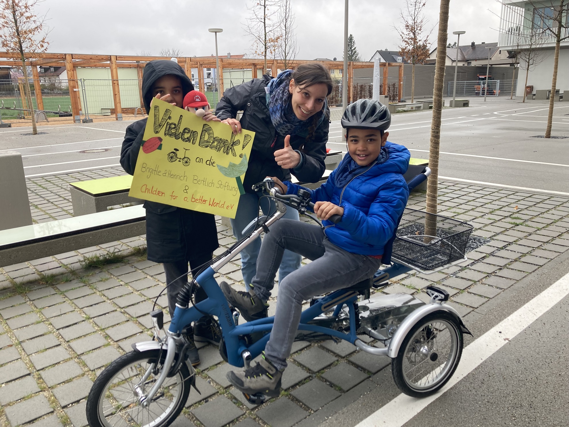 Zwei Schüler und eine Lehrerin halten beim Verkehrsunterricht ein Plakat in den Händen, auf dem sie sich für die Spenden bedanken